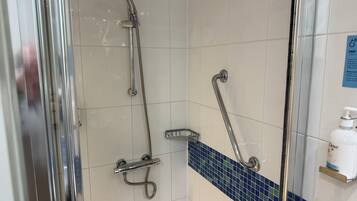 A shower area with a glass door, a handheld showerhead, a handheld showerhead, and a soap dispenser on a shelf.