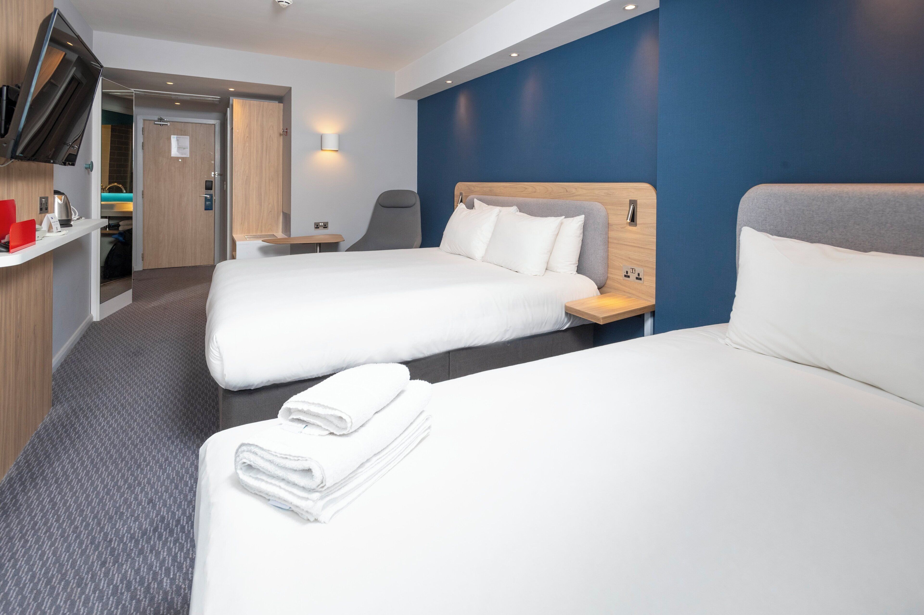 A hotel room with two beds, a desk, a chair, a TV, and a bathroom visible through an open door.