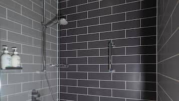 A shower area with a glass door, a handheld showerhead, and two Dove shampoo bottles on a shelf.