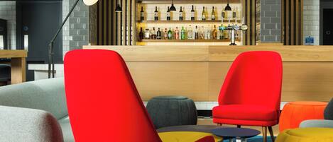 A modern bar area with a variety of seating options including red and grey chairs, a small round table, and a yellow ottoman.