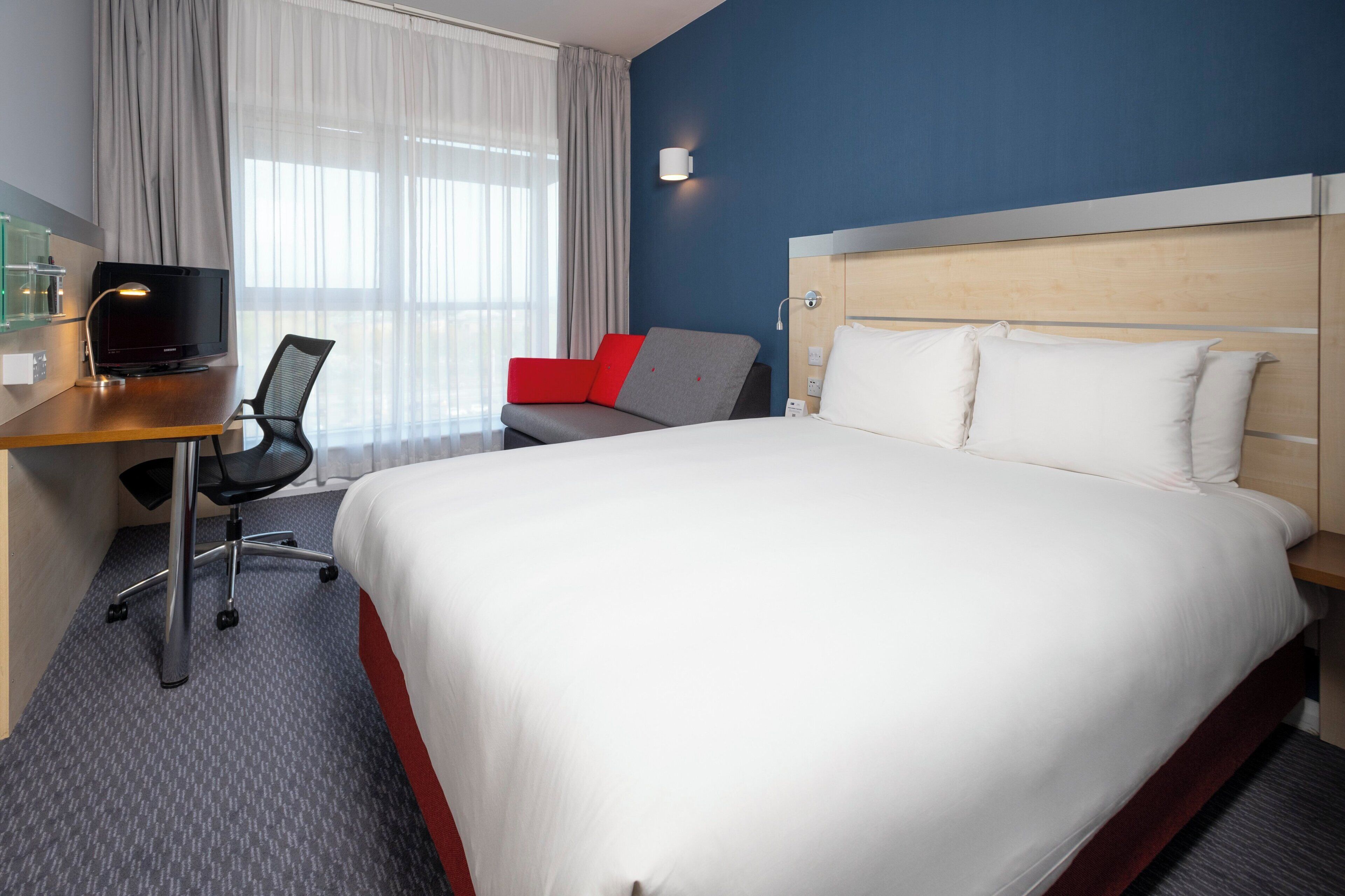 A hotel room with a large bed, a desk with a computer, a chair, and a red sofa.