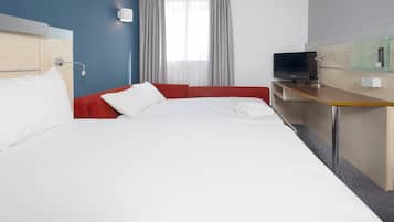Una habitación de hotel con una cama grande, un sofá rojo, un escritorio con televisor y una ventana con cortinas.