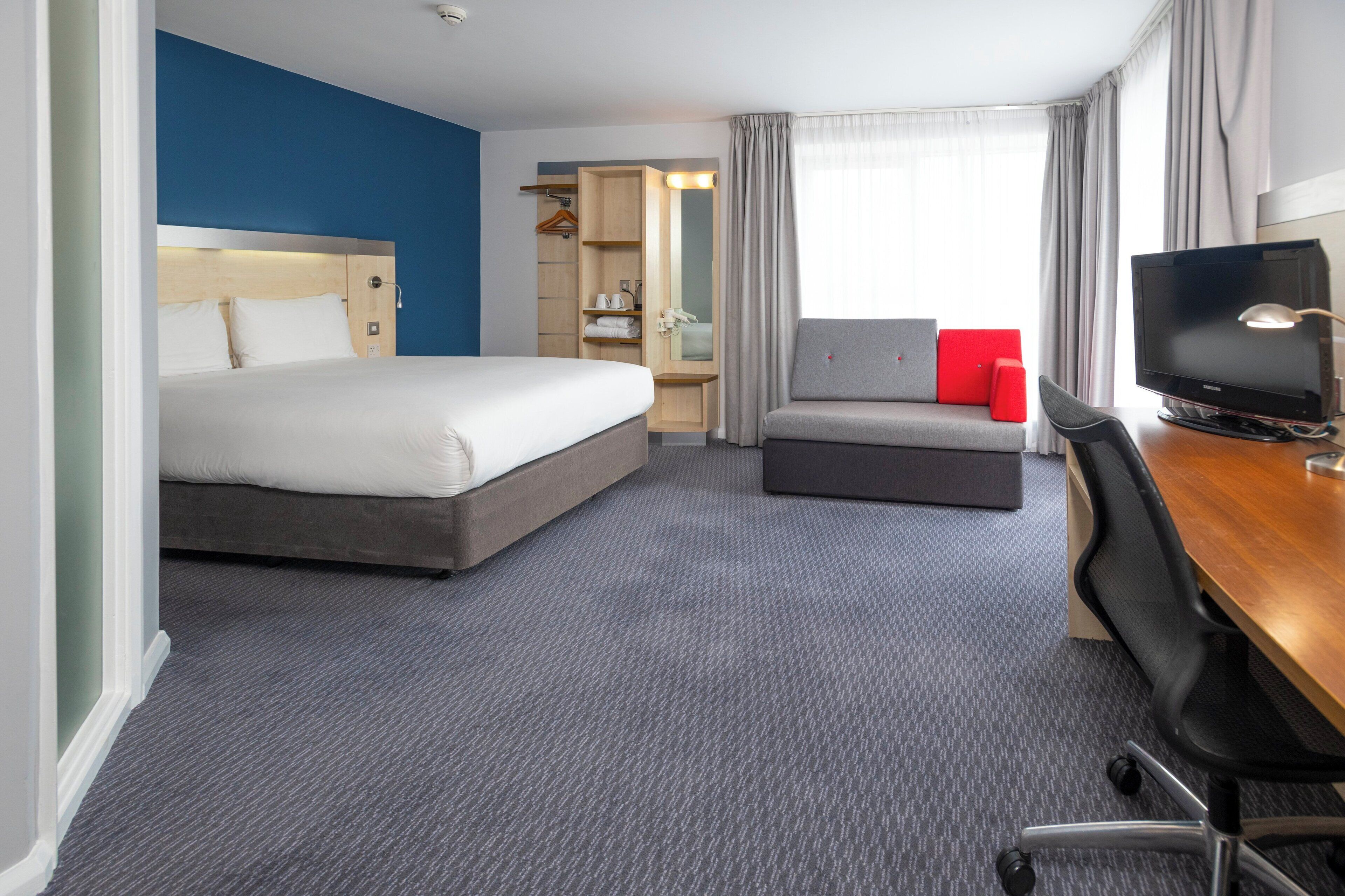 Une chambre d’hôtel avec un grand lit, un bureau avec un ordinateur, une télévision, un canapé et un dressing.