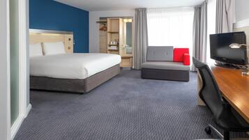 Une chambre d’hôtel avec un grand lit, un bureau avec un ordinateur, une télévision, un canapé et un dressing.
