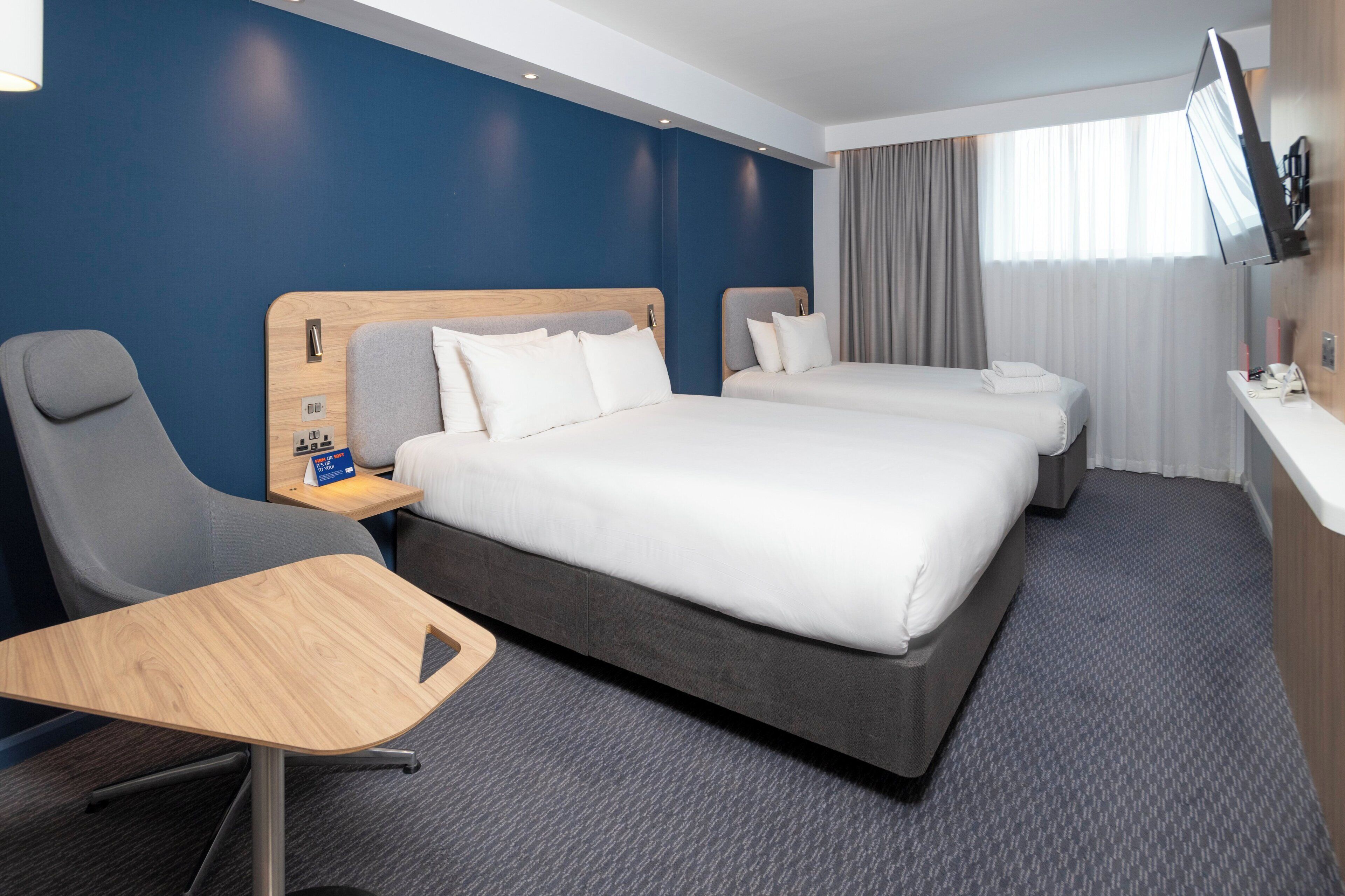 A hotel room with a bed, two bedside tables, a chair, a desk, and a TV.
