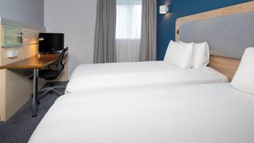 A hotel room with two beds, a desk with a computer, and a window with curtains.