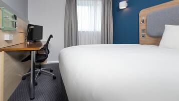Habitación de hotel con cama, escritorio con computadora, silla y ventana con cortinas.