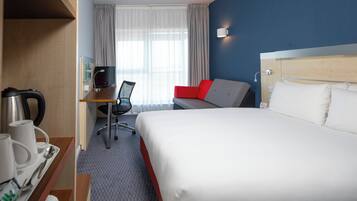 A hotel room with a bed, a desk with a chair, a coffee maker, and a TV.