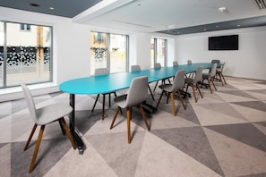 A conference room with a long table and chairs, large windows, and a flat-screen TV on the wall.
