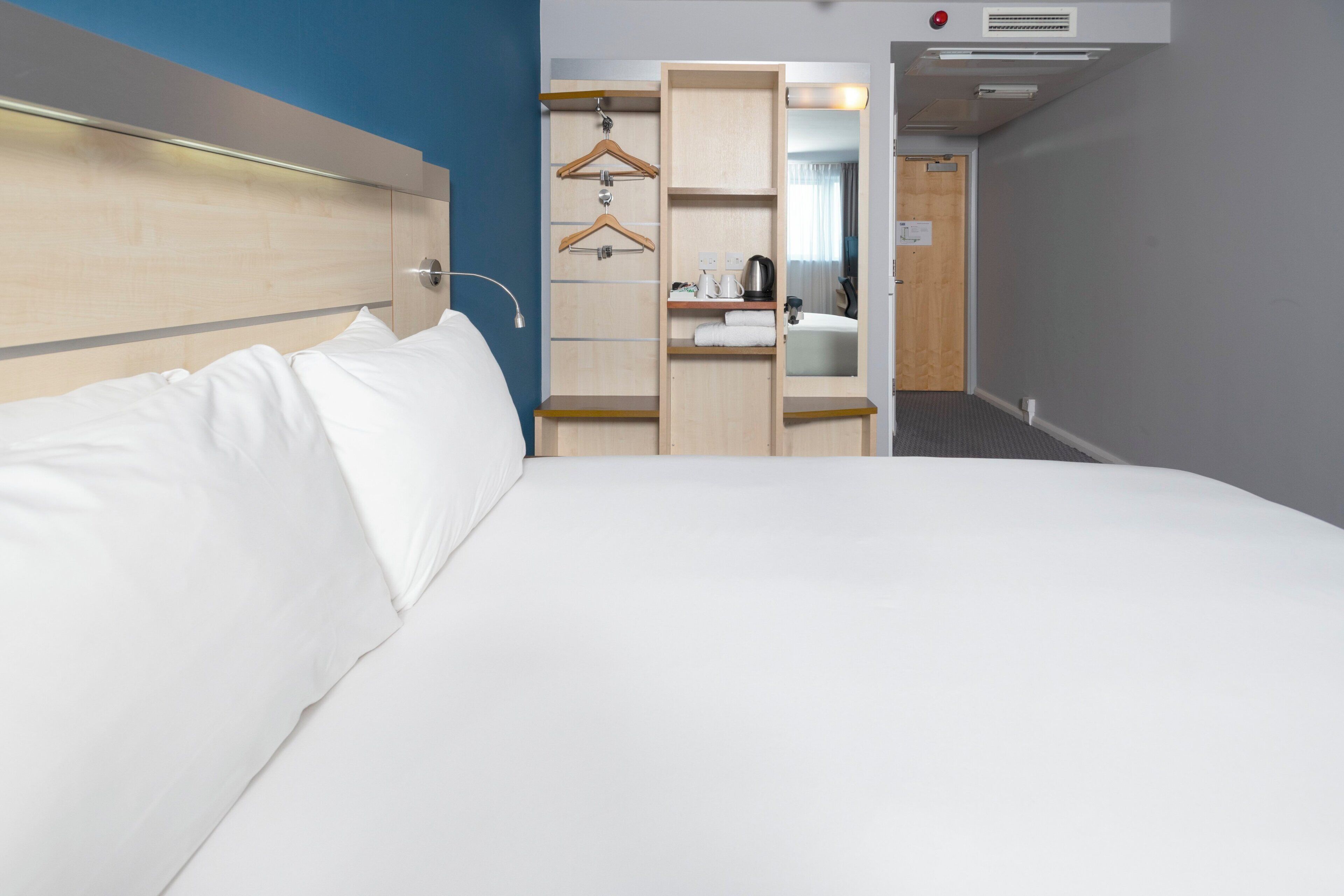 A hotel room with a bed, a wardrobe, a mirror, and a small bathroom area.