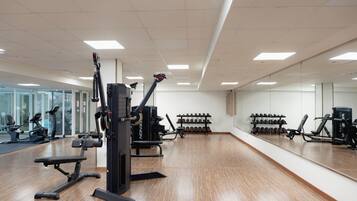 Un gimnasio con equipo de ejercicio, una banca y una estantería con mancuernas.