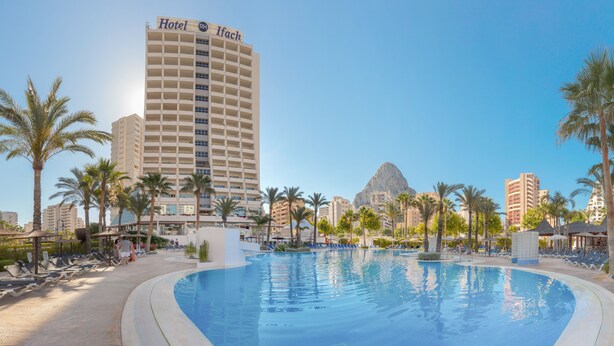 A hotel with a large pool surrounded by palm trees and lounge chairs.