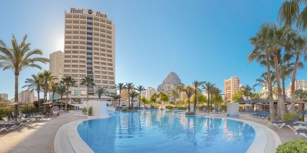 A hotel with a large pool surrounded by palm trees and lounge chairs.