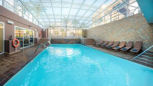 An indoor swimming pool with clear water, a glass ceiling, and a stone wall.