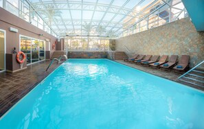 An indoor swimming pool with clear water, a glass ceiling, and a stone wall.