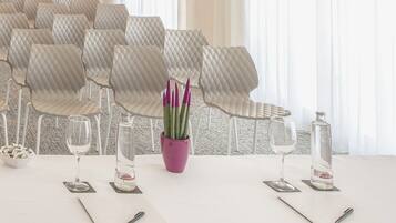 Una mesa de comedor con sillas blancas, un florero morado con plantas verdes y dos botellas de agua.