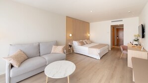 A modern hotel room with a sofa, a bed, a small round table, and a desk with a chair.