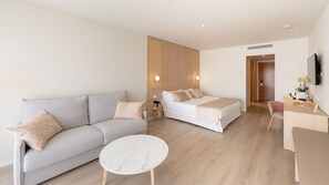 A modern hotel room with a sofa, a bed, a small round table, and a desk with a chair.