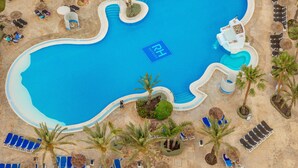 Una gran piscina rodeada de sillas de descanso y palmeras, con un edificio de techo de paja al fondo.
