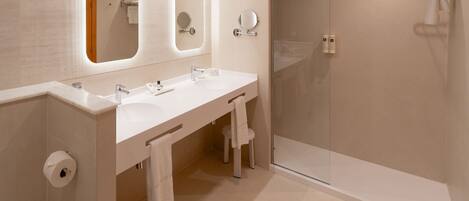 A modern bathroom with a double sink, a mirror, a towel rack, and a shower area.