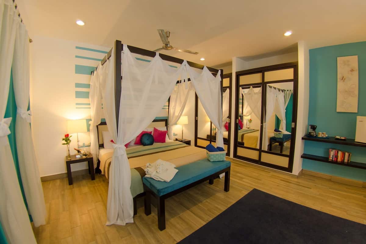 A bedroom with a four-poster bed, a bedside table, a bench, a mirror, and a view of another room.