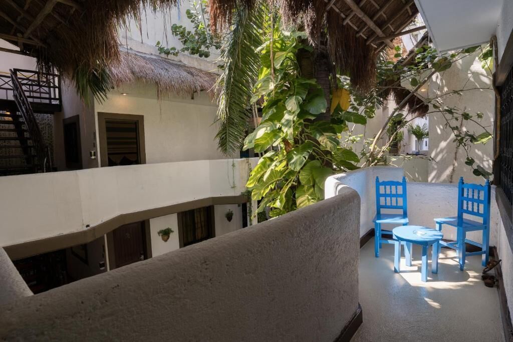 A covered outdoor area with a thatched roof, a staircase, and a seating area with blue chairs and a table.