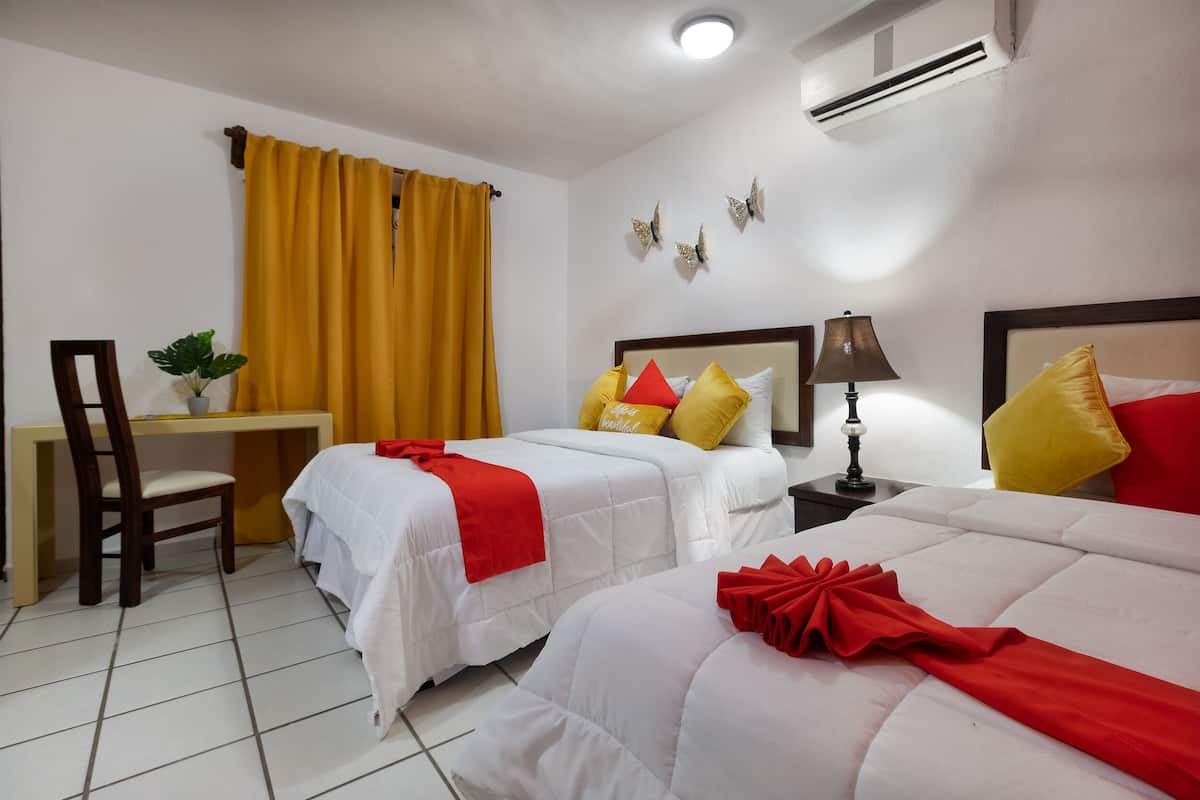 A hotel room with two beds, a desk, a chair, a lamp, and butterfly wall decor.