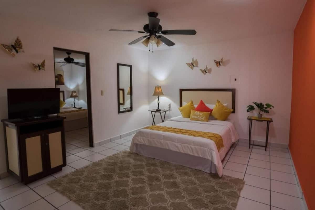 A bedroom with a bed, a television, a ceiling fan, a mirror, and decorative butterflies.