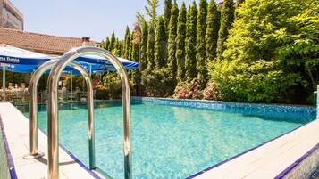 Piscina cristalina con escaleras metálicas, rodeada de un suelo de baldosas y abundante vegetación.