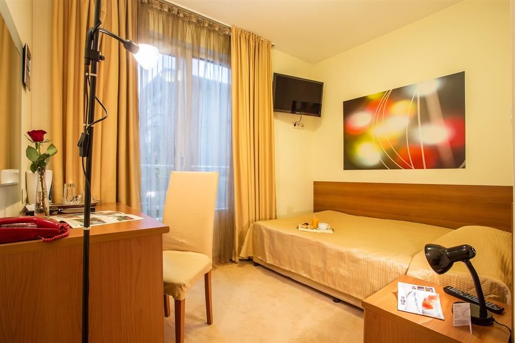 Une chambre d’hôtel comprenant un lit, un bureau avec un téléphone, une chaise, un téléviseur fixé au mur et un tableau.