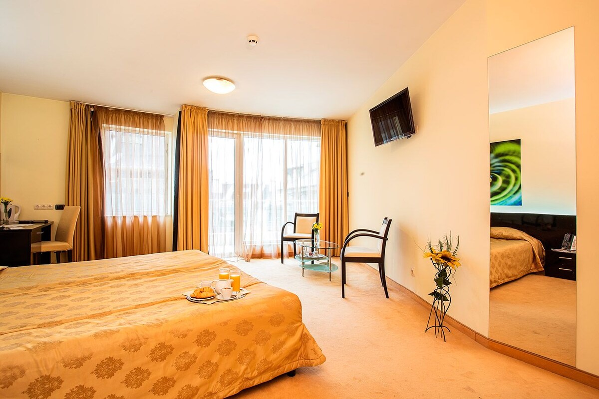 A hotel room with a bed, a desk, a chair, a TV, and a large mirror.