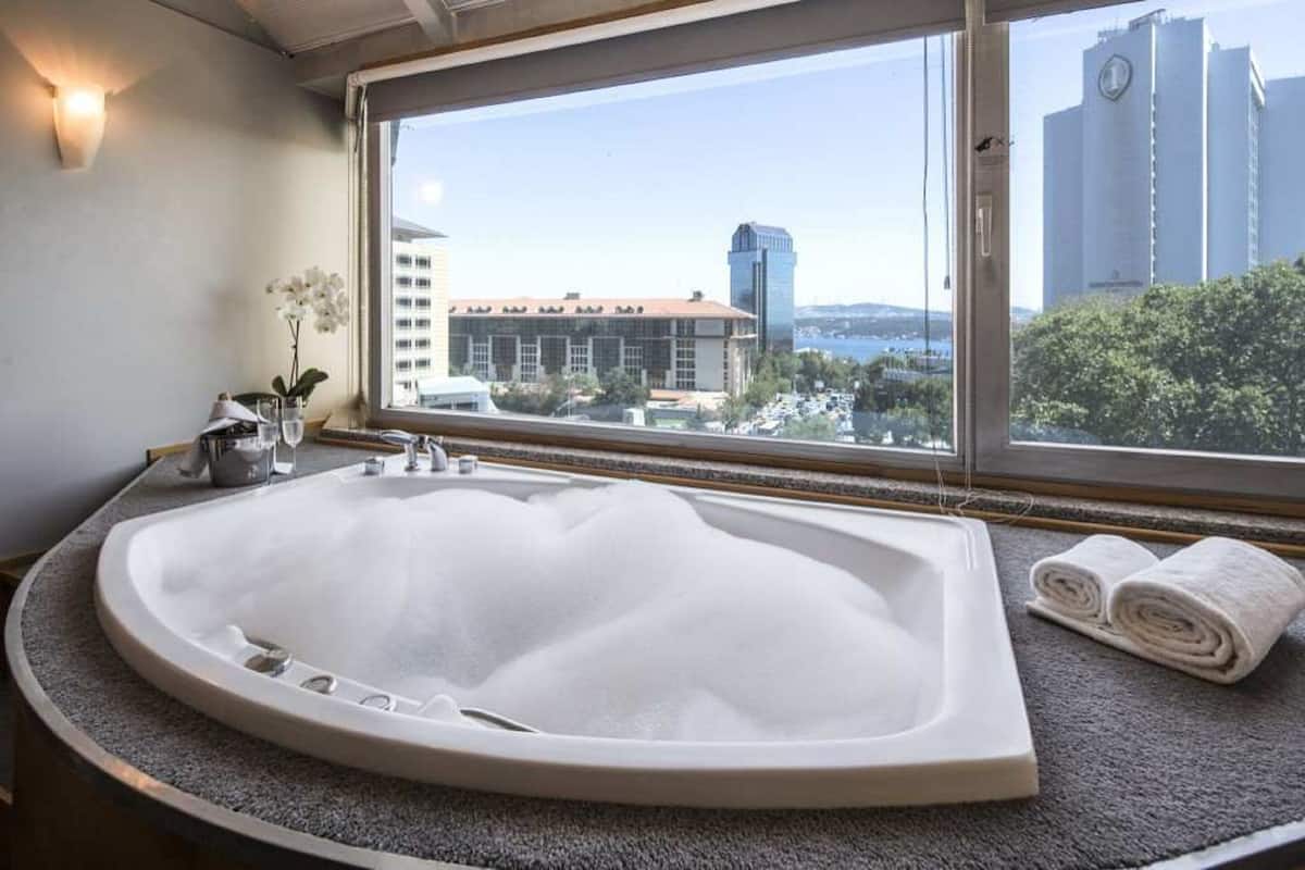 Ein modernes Badezimmer mit einer großen Badewanne, einem Fenster mit Stadtblick und einem Handtuchhalter.
