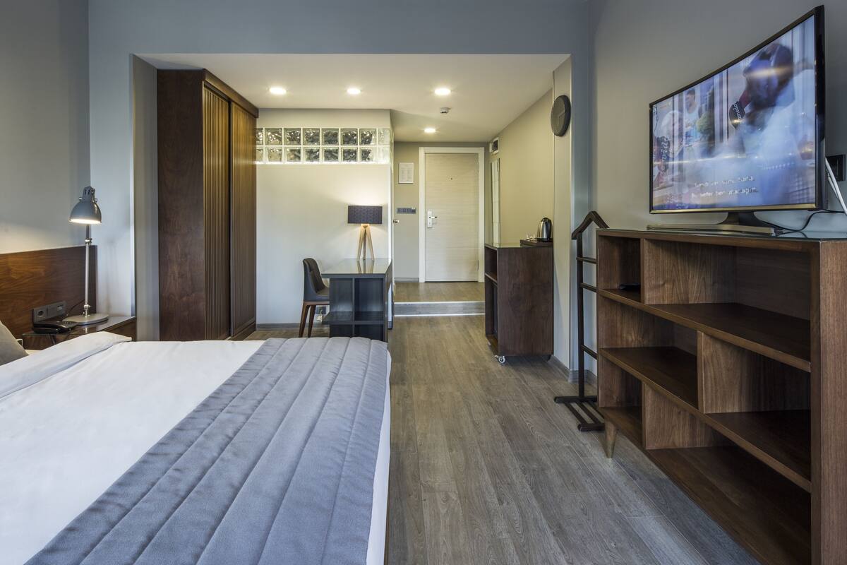 Ein Hotelzimmer mit Bett, Schreibtisch, Stuhl, Fernseher und einem Holzregal.
