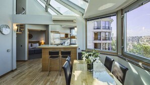 A modern kitchen with a central island, a dining area with a glass table, and a large window offering a city view. - Taxim Suites Residences Istanbul (Istanbul)