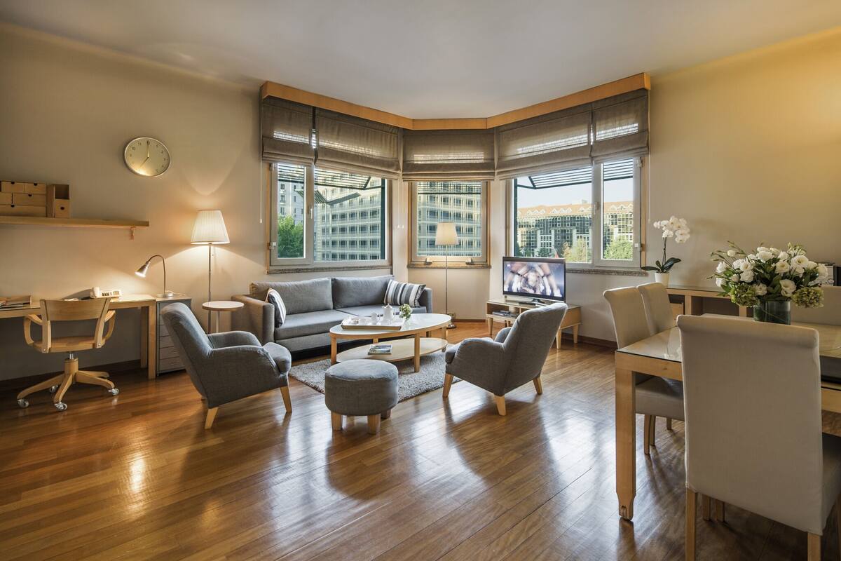 Ein modernes Wohnzimmer mit einer Couch, Sesseln, einem Couchtisch, einem Schreibtisch und einem Fernseher.