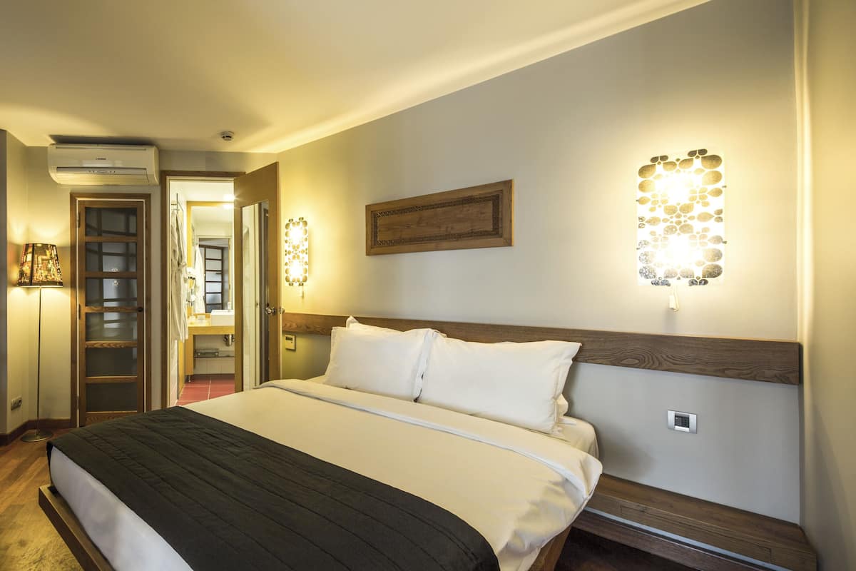 Ein Hotelzimmer mit Bett, Holz-Kopfteil, einer Wandleuchte und einer Tür zu einem Badezimmer.
