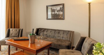 Una sala de estar con un sofá, una mesa de centro con una botella y vasos, y un cuadro en la pared.