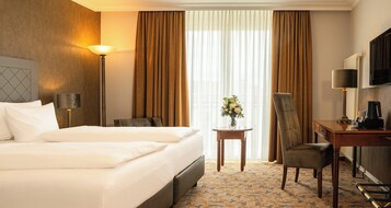 Ein Hotelzimmer mit einem großen Bett, einem Schreibtisch mit Stuhl, einer Lampe und einem Fernseher.
