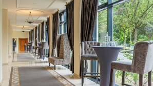 A hotel lobby with a long corridor, plush seating, large windows, and a view of greenery.