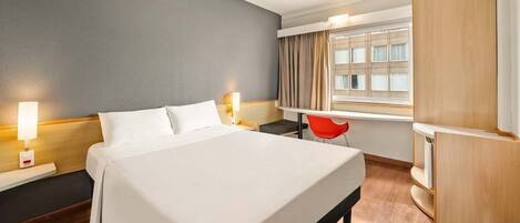 A hotel room with a bed, bedside tables, a desk, a chair, a wardrobe, and a window with curtains.