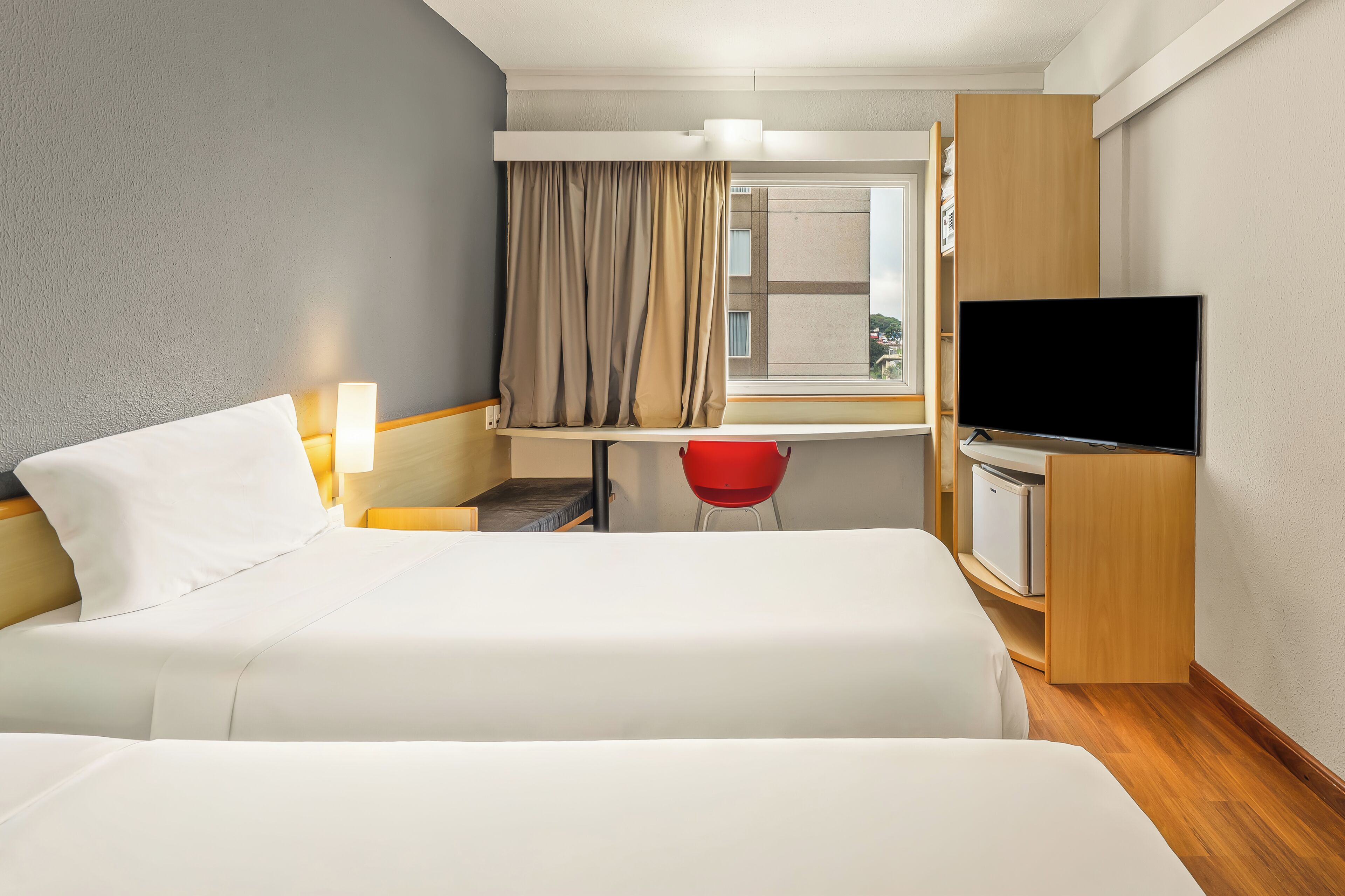 Habitación de hotel con cama, escritorio con silla, televisor y ventana con cortinas.