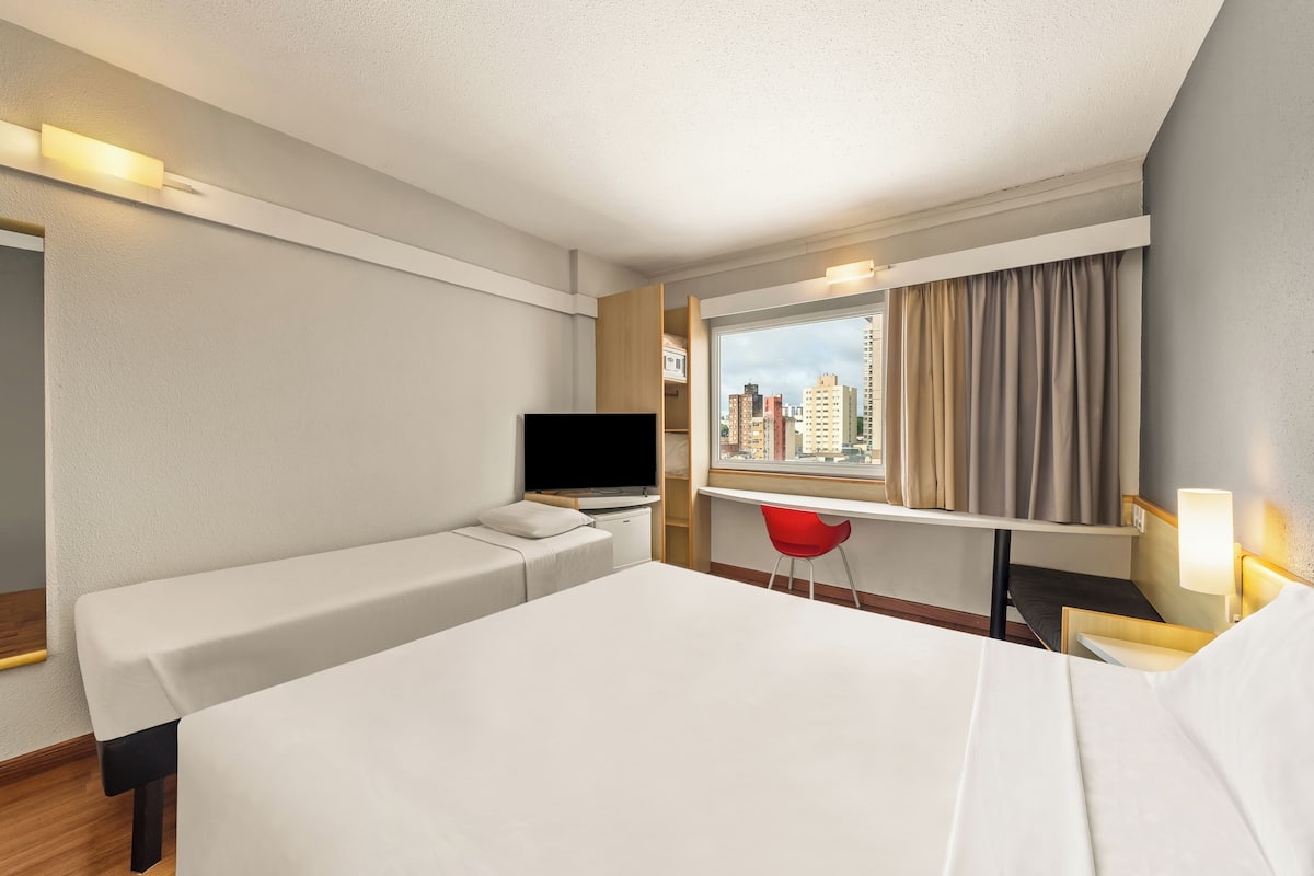 A hotel room with a bed, a desk, a TV, and a window with curtains.