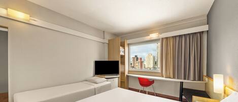 A hotel room with a bed, a desk, a TV, and a window with curtains.