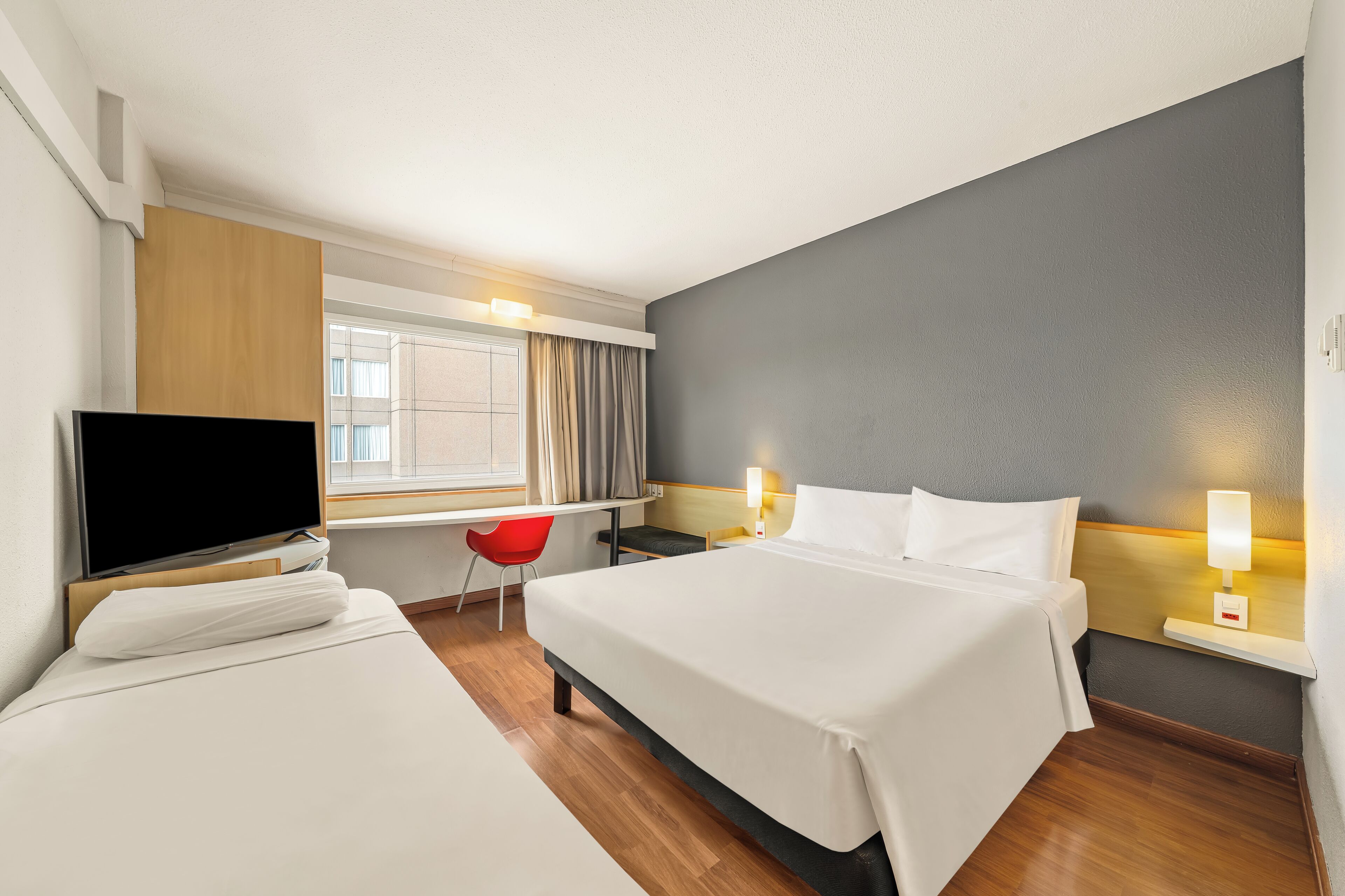 A hotel room with two beds, a TV, a desk, and a red chair.