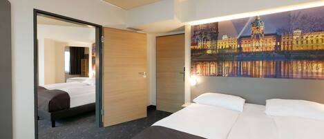 A hotel room with a bed, a mirror, a door, and a wall with a cityscape painting.