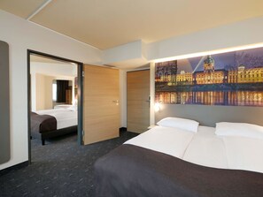 Quarto de hotel com cama, espelho, porta e parede com pintura de paisagem urbana.