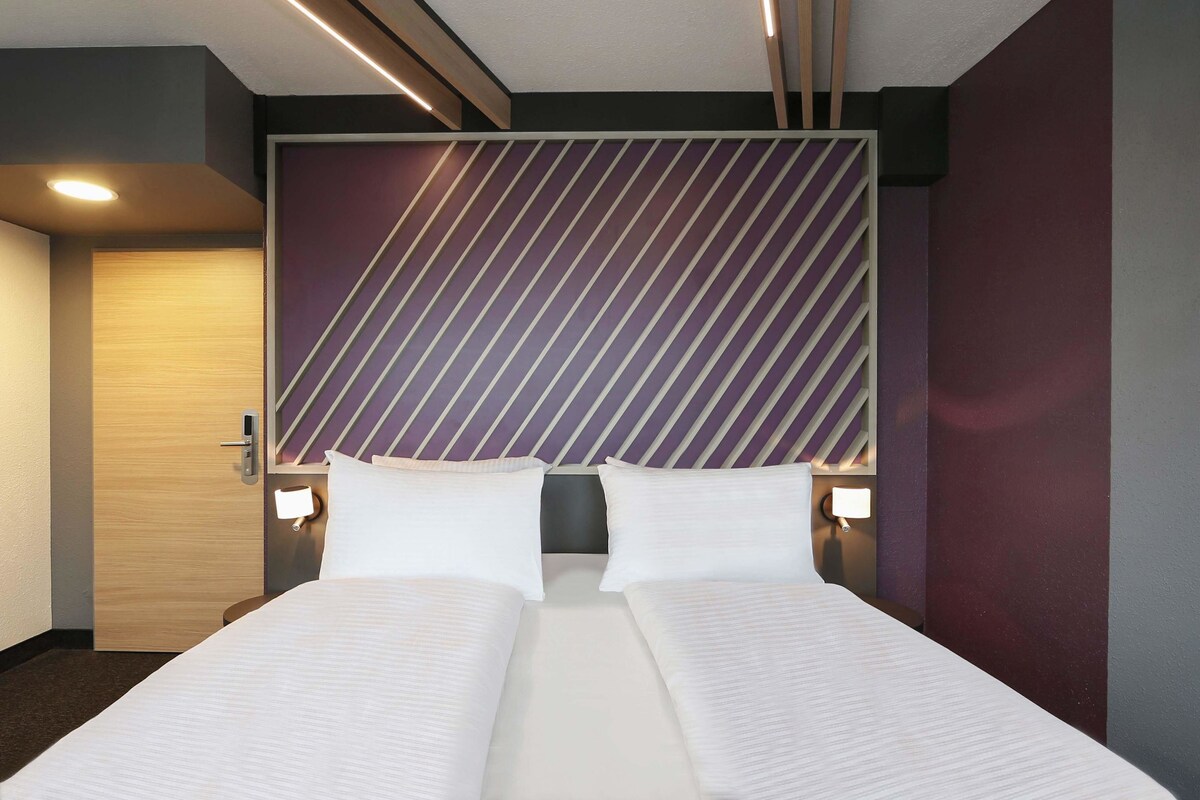 Une chambre d’hôtel avec un grand lit, deux tables de chevet et une tête de lit moderne ornée de rayures diagonales.