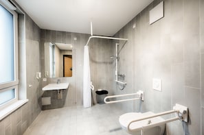 Enjoy a refreshing shower in the walk-in shower with handheld showerhead, complemented by a convenient sink and mirror, and a toilet with safety rail.
