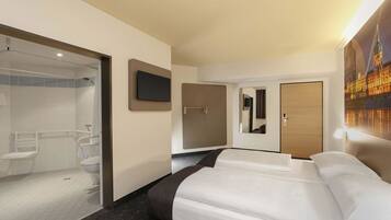 Ein Hotelzimmer mit Bett, Wandfernseher, Badezimmer mit Dusche, Toilette und Spiegel.