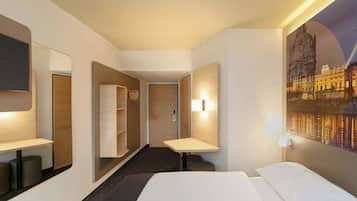 A hotel room with a bed, a desk, a mirror, a wardrobe, and a painting of a cityscape.